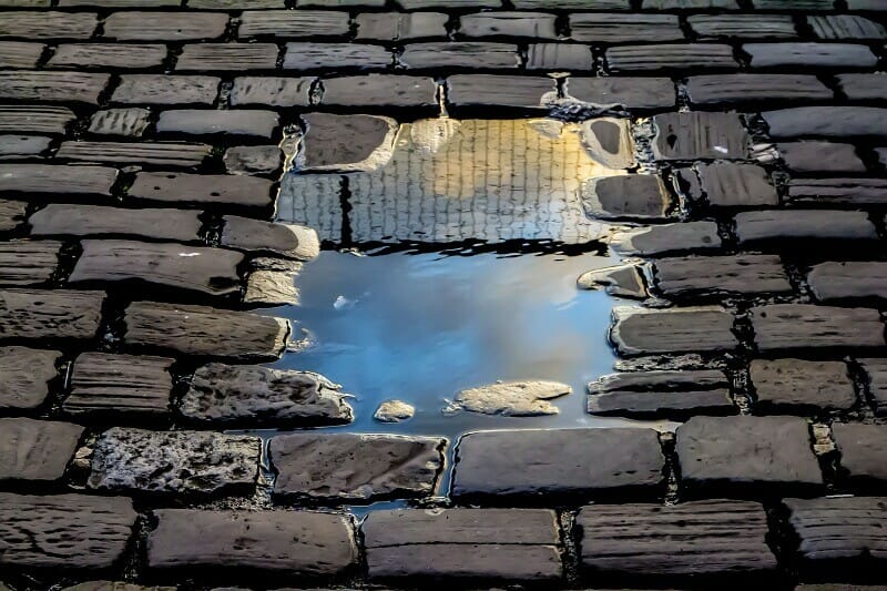 Reflection of a prison fence in a puddle of water on a stone block